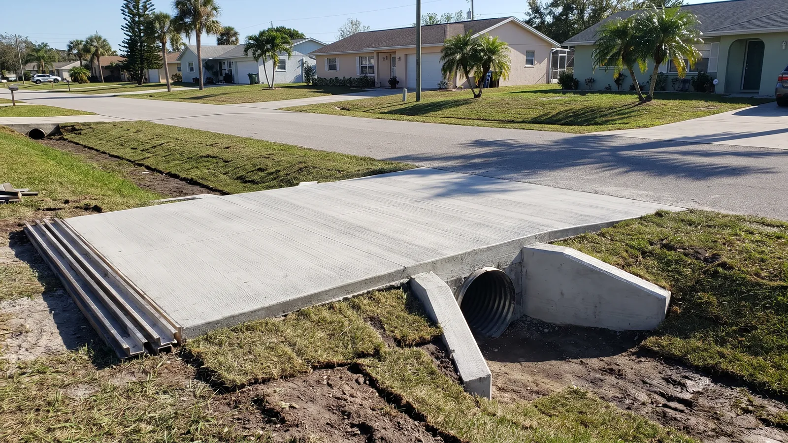 New concrete driveway apron crossing a roadside swale on a corrugated culvert pipe with poured mitered end sections in Palm Bay
