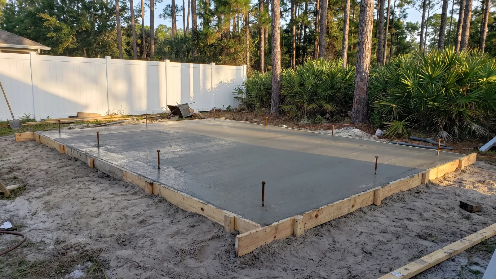 Reinforced concrete shed slab with turned-down edges and anchor bolts set in a Florida backyard